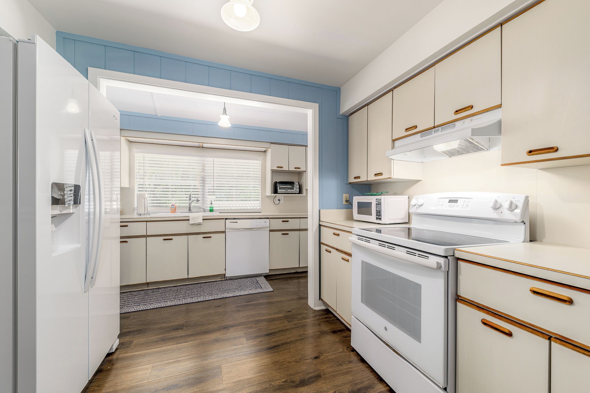 Une cuisine de taille réduite, avec des appareils électroménagers blancs, des poignées en bois et un mur d’accent bleu.