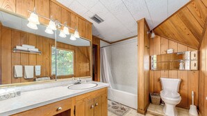 Ein Badezimmer aus Holz mit großem Spiegel, Waschtisch, Badewanne und Toilette.