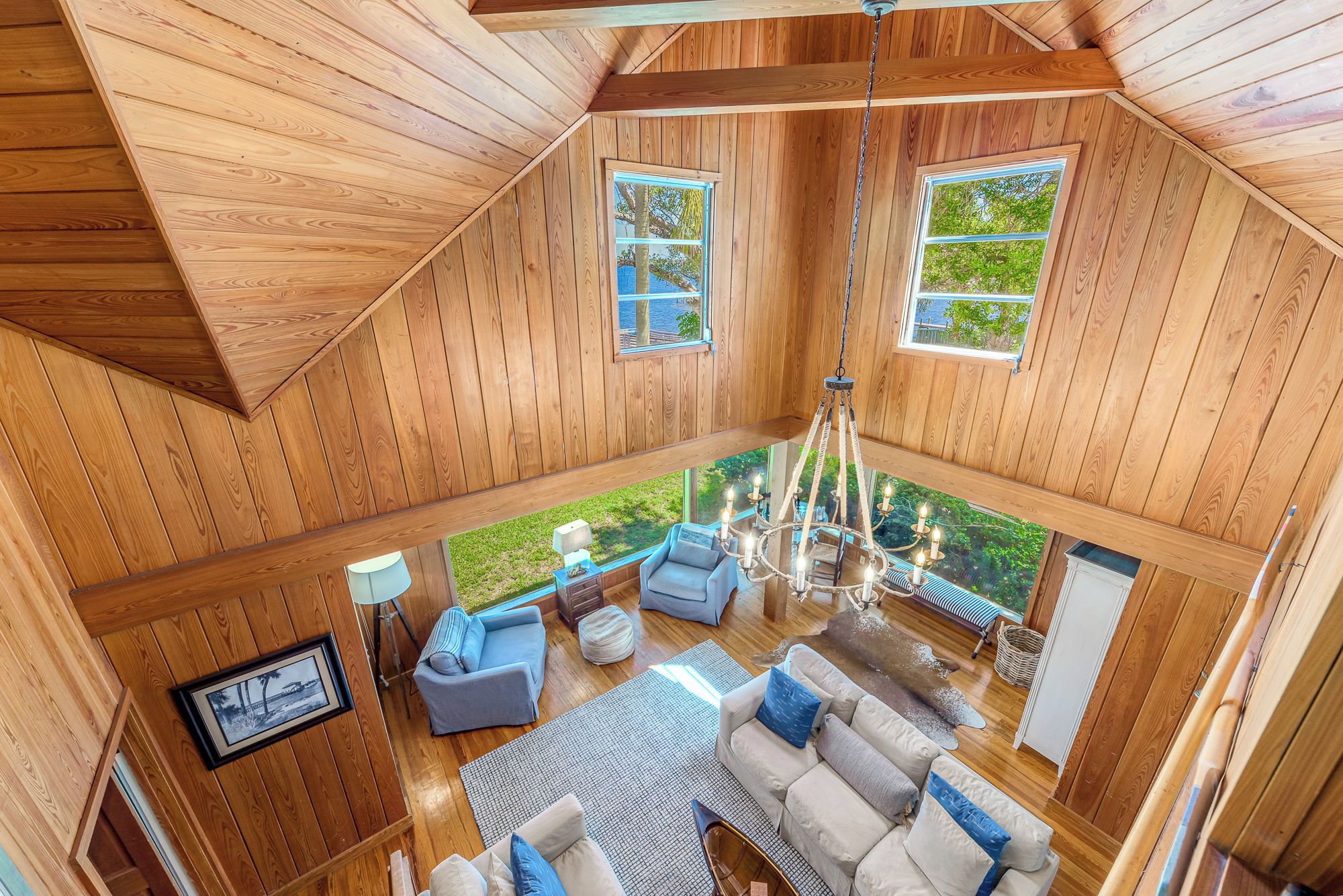 Un intérieur en bois aux hauts plafonds, avec un espace salon central, de grandes fenêtres et un lustre.