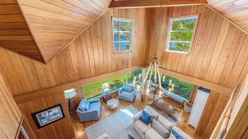 Un intérieur en bois aux hauts plafonds, avec un espace salon central, de grandes fenêtres et un lustre.