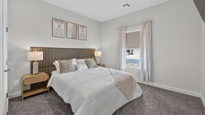 Quarto com cama, mesas de cabeceira, luminárias, janela com cortinas e quadros na parede.