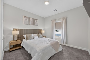 Un dormitorio con cama, mesitas de noche, lámparas, una ventana con cortinas y decoración en la pared.