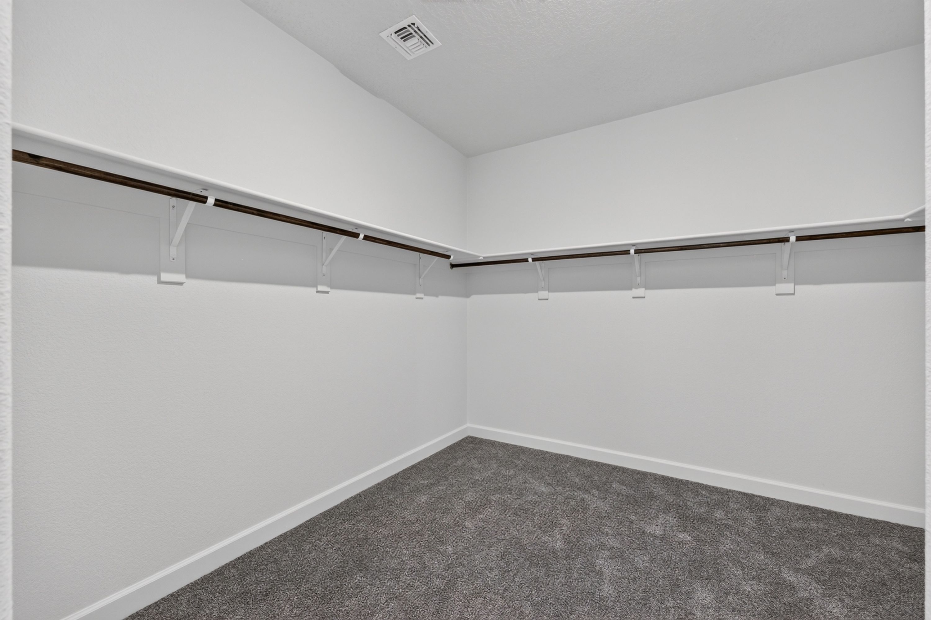 A room with white walls, a grey carpet, and a ceiling vent.