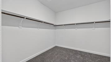 A room with white walls, a grey carpet, and a ceiling vent.