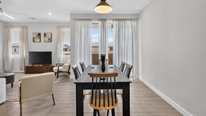 Uma sala de estar moderna com área de refeições, TV de tela plana e uma janela grande com cortinas.