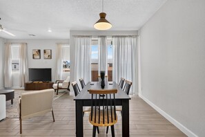 Una sala de estar moderna con comedor, televisor de pantalla plana y un amplio ventanal con cortinas.
