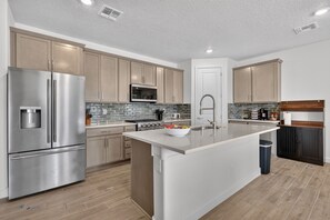 A modern kitchen with stainless steel appliances, a central island, and a tiled backsplash.