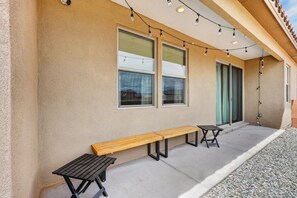 A building exterior with a concrete patio, two wooden benches, and string lights.