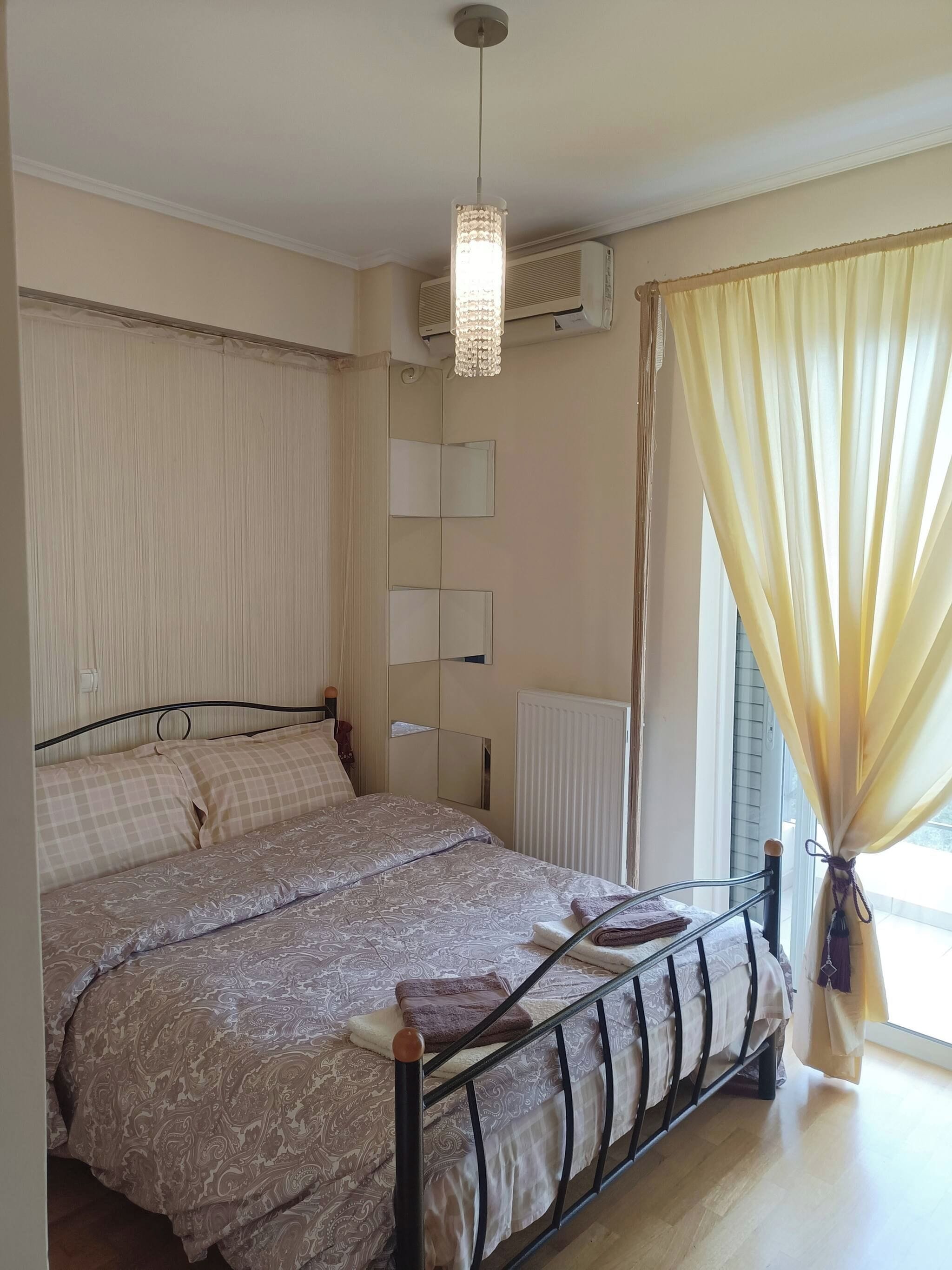A bedroom with a bed, a hanging light fixture, a radiator, and a window with curtains.