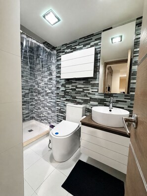 Et moderne badeværelse med bruser, toilet, håndvask og spejl.