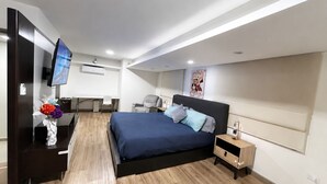 Een moderne slaapkamer met een bed, nachtkastjes, een bureau, een stoel en een televisie.