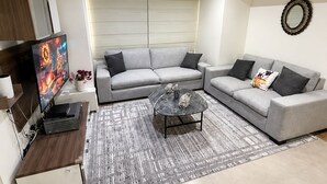 Een moderne woonkamer met een grijze modulaire bank, een bijzettafeltje, een flatscreen televisie en een decoratieve spiegel.