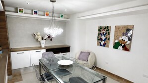 Een moderne eetruimte met een tafel met glazen blad, metalen stoelen en een witte vaas met bloemen.