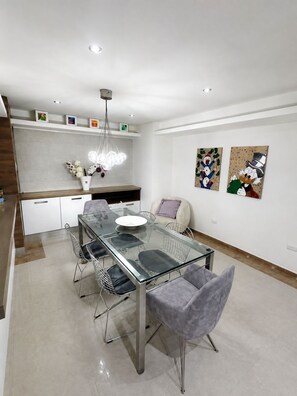 Et moderne spiseområde med et bord med glasplade, metalstole og en hvid vase med blomster.