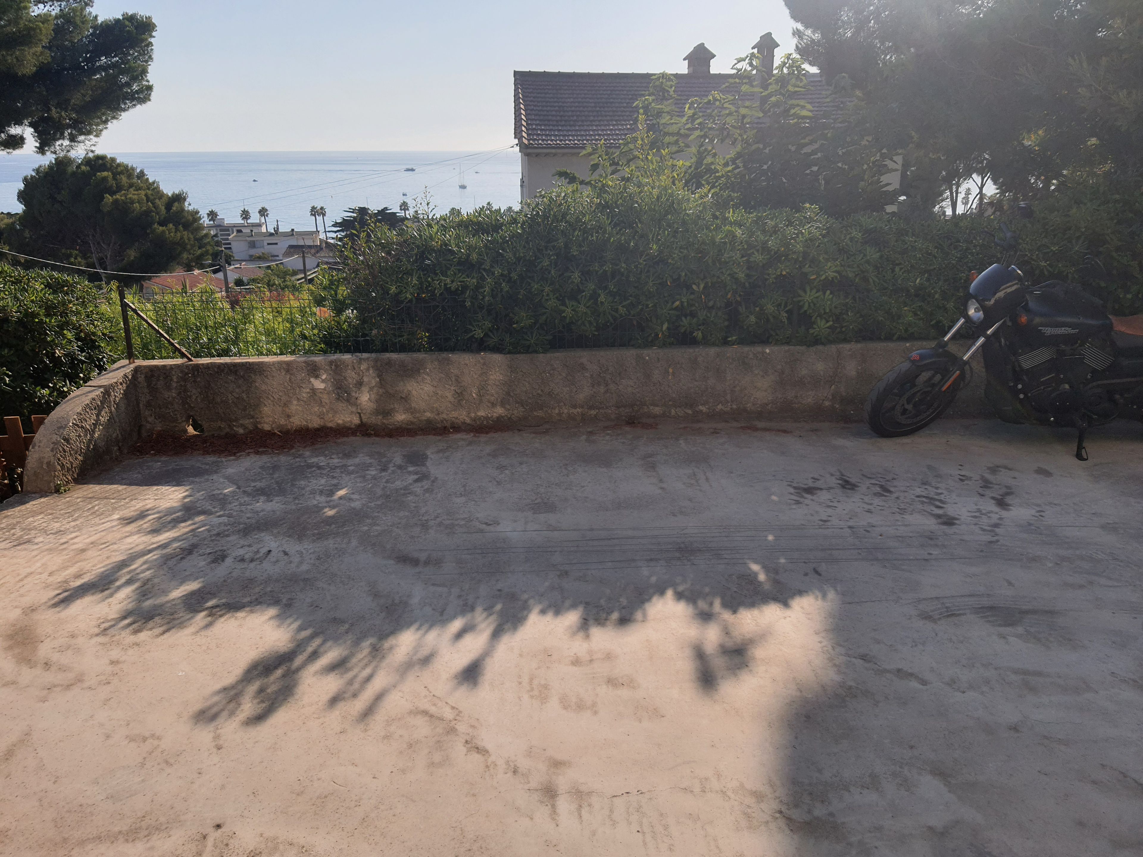 A concrete rooftop with a motorcycle parked, overlooking a coastal area with buildings and trees.