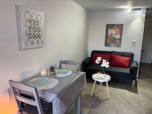 Ein Wohnzimmer mit Esstisch, Stühlen, einer roten Couch und einem Poster an der Wand.