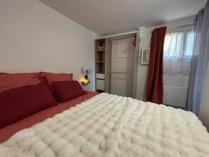 Una camera da letto con un letto, un armadio, un comodino con una lampada e una finestra con tende.
