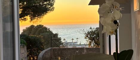 Una habitación con vistas al mar al atardecer, una mesa con una vela y una planta en maceta.