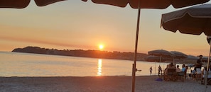 Ein Strandbild mit Sonnenuntergang, Sonnenschirmen und Menschen.