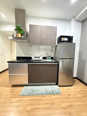 A modern kitchen with a built-in stove, a refrigerator, and wooden cabinets. - Cozy Studio Unit condo in the heart of Makati with a perfect city view. (Makati)