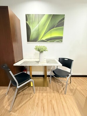A dining area with a table, two chairs, a vase with green plants, and a wall-mounted abstract art piece. - Cozy Studio Unit condo in the heart of Makati with a perfect city view. (Makati)