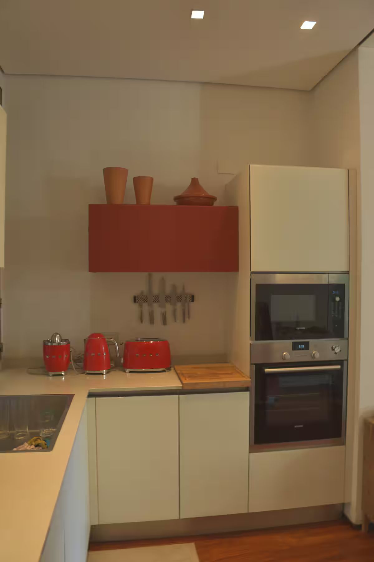Cocina compacta con microondas, tostadora y teteras rojas sobre la encimera.
