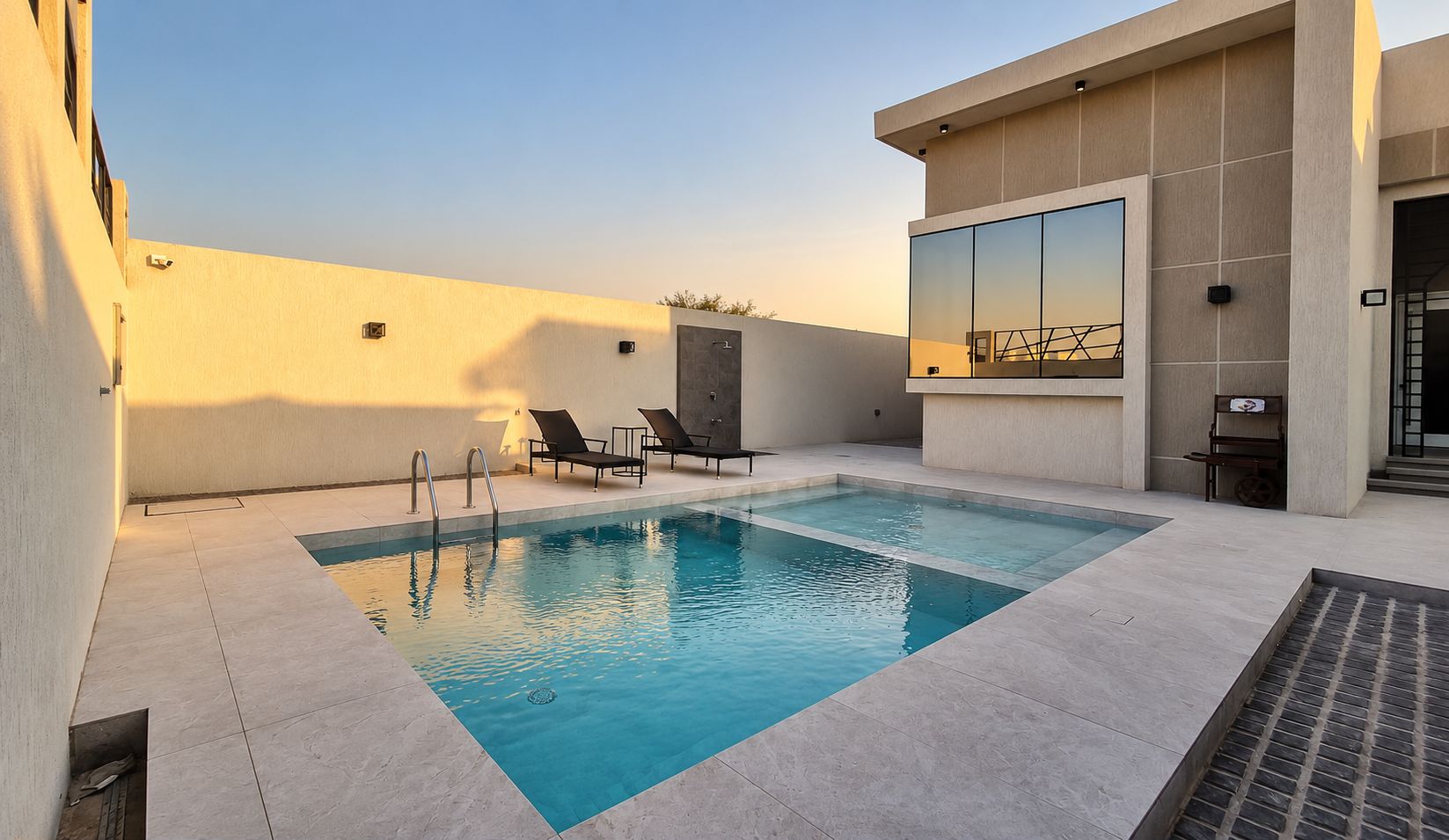 A rooftop swimming pool with a clear view of the sky, a modern building with large windows, and a few lounge chairs.