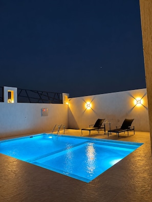 An outdoor swimming pool with lounge chairs and wall-mounted lights.