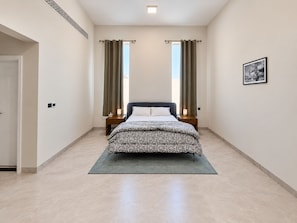A bedroom with a bed centered, two bedside tables with lamps, a door on the left, and a framed picture on the wall.