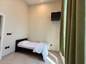 Una cama individual en una habitación con televisor instalado en la pared y una puerta con interruptor de luz.