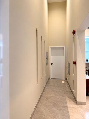 A hallway with a door at the end, light-colored walls, and a tiled floor.