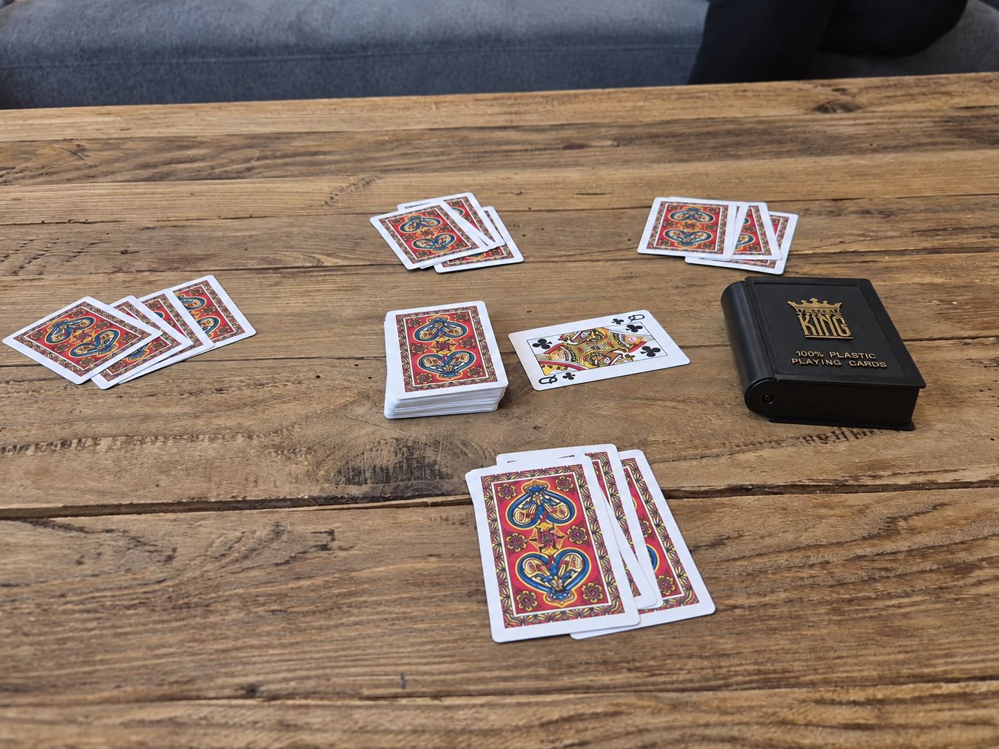 Ein Holztisch mit Spielkarten und einer schwarzen Box mit dem Aufdruck '100% Plastik Spielkarten'.