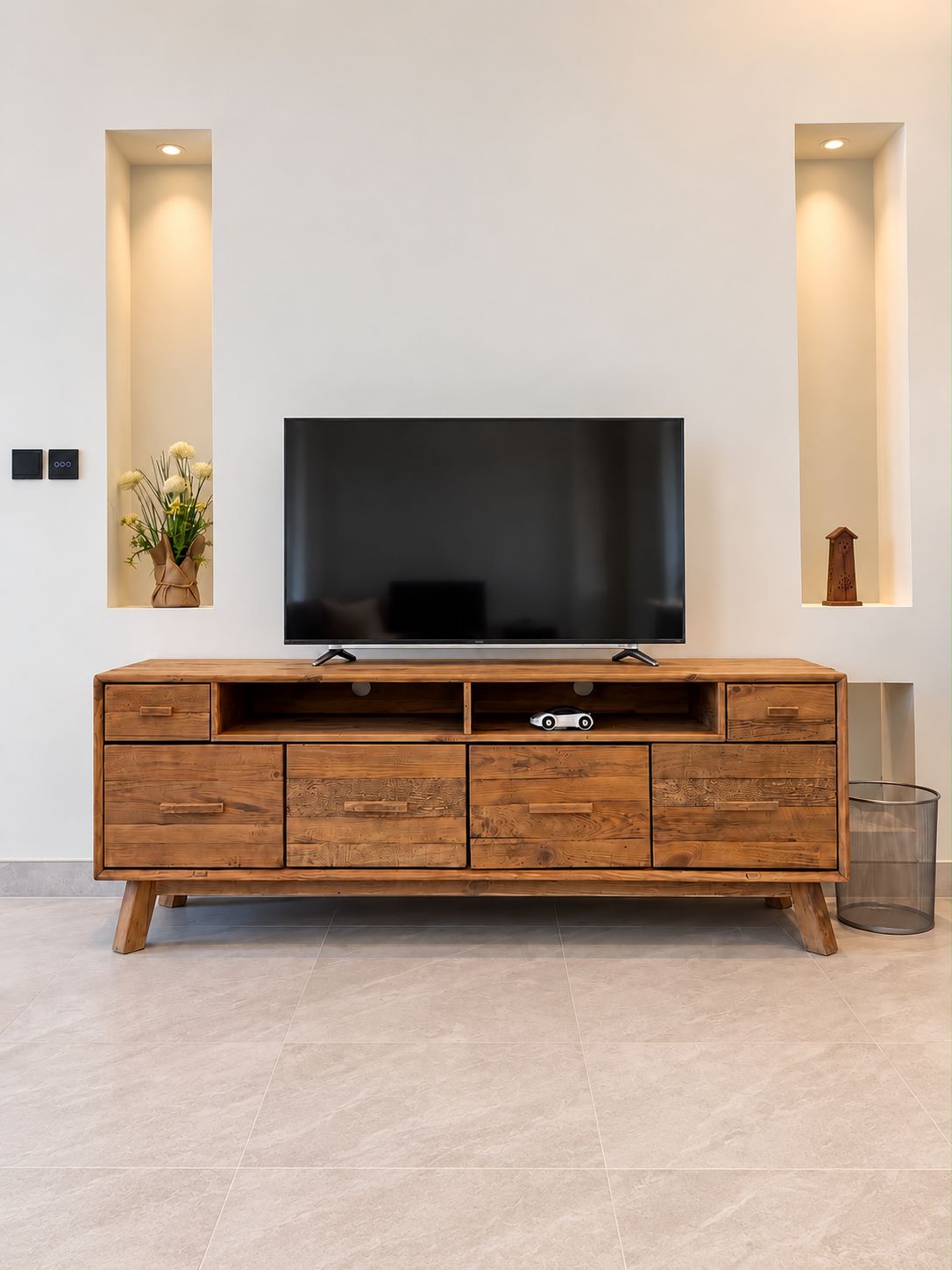 Ein modernes Wohnzimmer mit einem flachbildfernseher an einer Holzeinrichtung, zwei Wandleuchten und einer kleinen Pflanze.