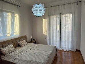 Un dormitori amb llit, taula de nit, làmpada, cortines i llum penjant.