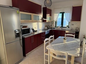 A modern kitchen with stainless steel appliances, a dining table with chairs, and a view of the sea through the window. - Spacious 3 Bedroom Apartment with Stunning Sea View (Saranda)