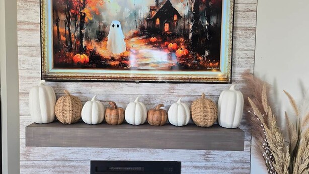 Una chimenea con un fuste rústico, un cuadro enmarcado encima y calabazas decorativas sobre el fuste.