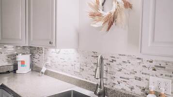 Una cocina con dos lavamanos de acero inoxidable, un protector contra salpicaduras blanco y un adorno decorativo en la pared.