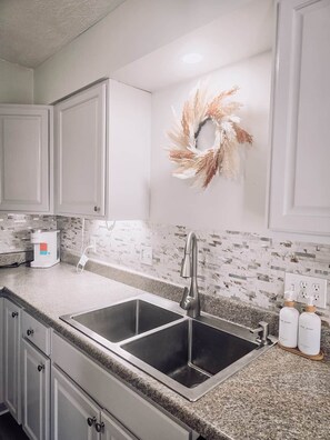 Una cocina con dos lavamanos de acero inoxidable, un protector contra salpicaduras blanco y un adorno decorativo en la pared.