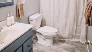 Un baño con inodoro blanco, lavabo con espejo y cortina de ducha.