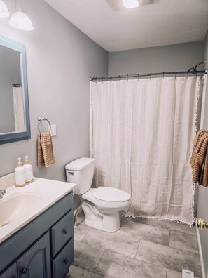 Un baño con inodoro blanco, lavabo con espejo y cortina de ducha.