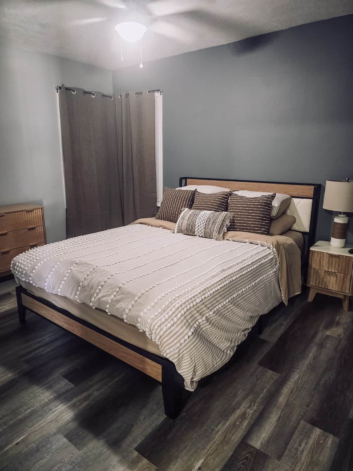 Un dormitorio con cama, mesitas de noche, lámpara y ventana con cortinas.