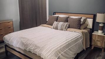 Un dormitorio con cama, mesitas de noche, lámpara y ventana con cortinas.