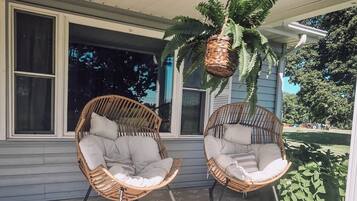 A covered porch with two wicker chairs and a hanging basket.