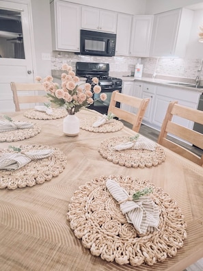 Una mesa de comedor con manteles individuales, un jarrón de flores y servilletas a rayas.