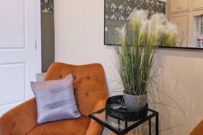 A room with a brown chair, a white door, a framed picture on the wall, and a potted plant on a small table. - 5-Bed Home | 10 Mins to Etihad & City Centre (Greater Manchester)