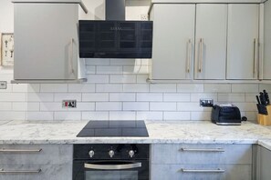 A kitchen with white cabinets, a black range hood, a built-in oven, and a toaster on the countertop. - 5-Bed Home | 10 Mins to Etihad & City Centre (Greater Manchester)
