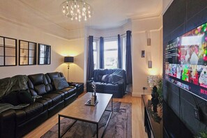 Un salon moderne avec un canapé en cuir noir, une table basse et un téléviseur à écran plat fixé au mur.
