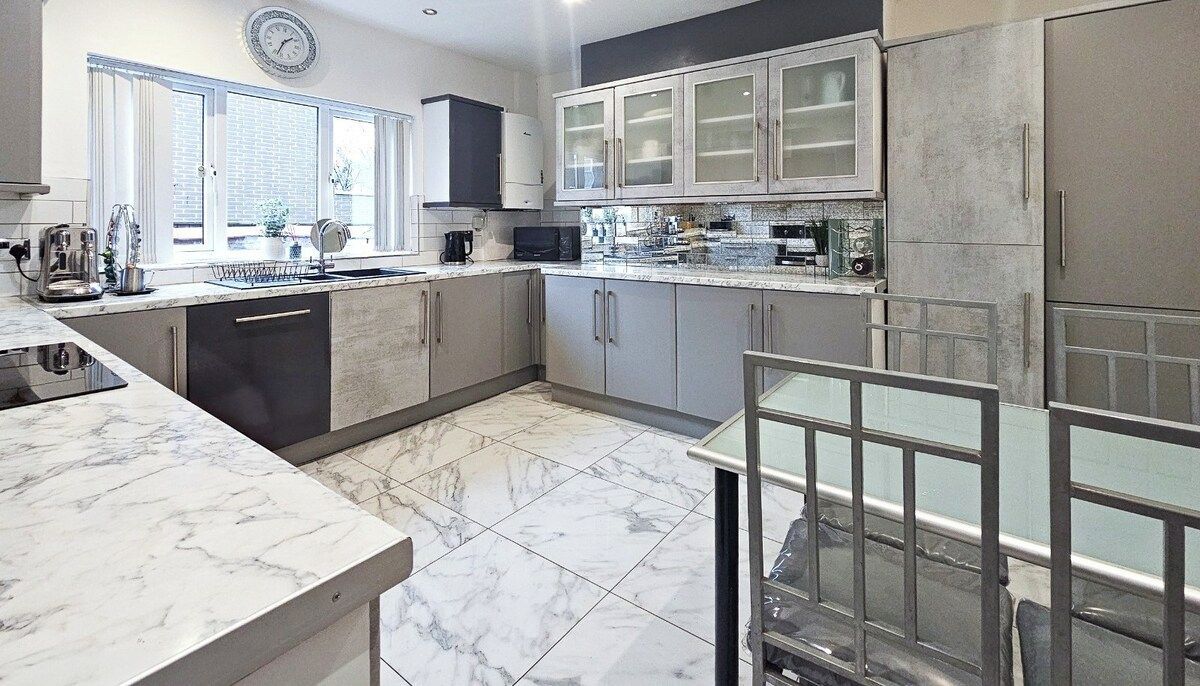 A modern kitchen with marble countertops, a dishwasher, and a dining area with a glass table.