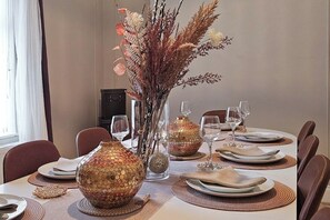 Une table à manger dressée pour quatre personnes, agrémentée d’un centre de table décoratif, de verres transparents et de sets de table en fibres tressées.