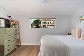A bedroom with a bed, a dresser, a window with a view of a house, and a ceiling light. - Venice Beach 1-Bedroom Apartment w/ Roof Top Deck (Los Angeles)